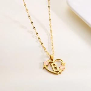 Detail of gold heart pendant with letter B and pink enamel flowers on a gold chain