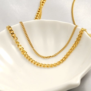 Close-up of gold stainless steel Cuban chain and curb chain layers in shell tray