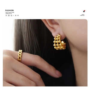 Close-up of gold beaded C-shape earrings and matching chain ring on a fashion model