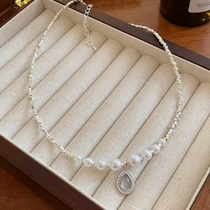 Detail of silver chain necklace with pearls and a teardrop blue gemstone pendant