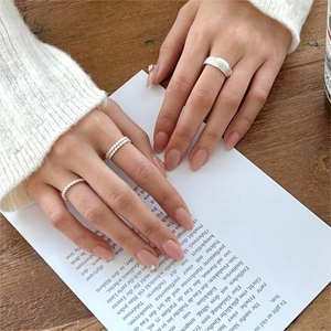 Close-up of three stackable 925 silver zircon rings on model fingers against wood background