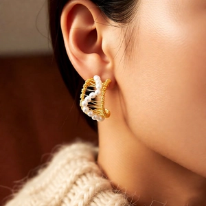 Macro shot of French vintage 18k gold-plated C-shaped earrings with pearl accents on model