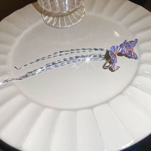 Macro detail of purple butterfly ear cuff with silver tassels on white ceramic plate