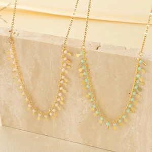 Bohemian gold tassel necklaces with pink and blue beads on a beige textured stone base