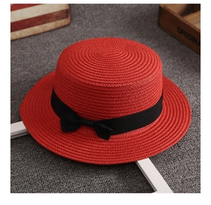Dettaglio di un cappello di paglia rosso a corona piatta con nastro nero e fiocco