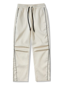 Detail of khaki techwear pants featuring black side stripes and pleated knee construction