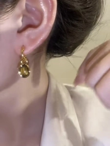 Close-up of gold plated oval tiger eye stone earrings on ear for a retro luxury look