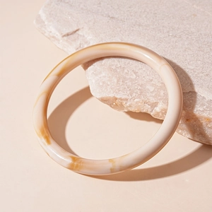 Detailed macro view of beige marbled acrylic resin bangle on a natural stone base