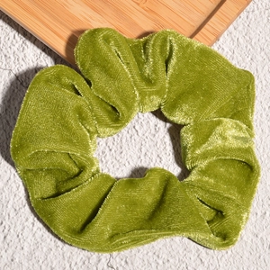 Detailed view of an avocado green velvet scrunchie on a decorative wooden tray