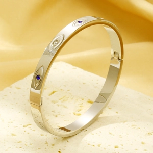 Silver evil eye titanium steel bangle with blue crystals on a premium gold silk background