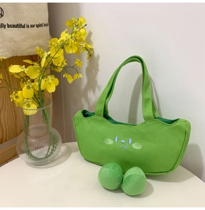 Detail of green canvas tote with blue cartoon embroidery and matching fuzzy pom pom charms