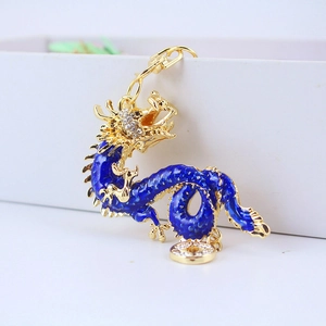 Golden metal dragon keychain with blue enamel and rhinestones on a white box