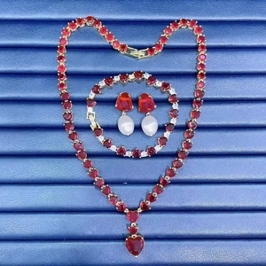 Elegant gold jewelry set with red heart gems and pearls on a blue textured background