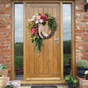 Floral wreath detail with pink hydrangea, greenery, and burlap bow on a wooden door