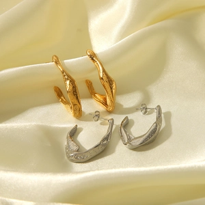 Close-up of gold and silver irregular lava texture C-shape earrings on silk fabric