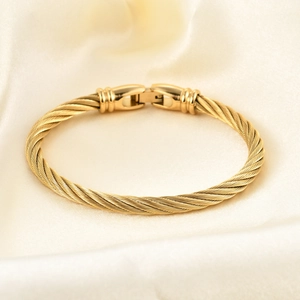 Detail of golden cable twist bangle featuring a polished clasp on elegant silk fabric