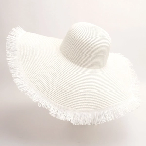 Detailed close-up of white woven straw beach hat with fringe trim and wide brim design