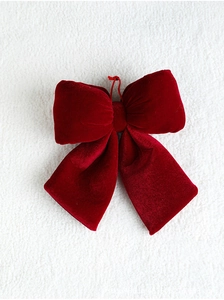 Close-up of a large red velvet Christmas bow with hanging rope on a soft textured background