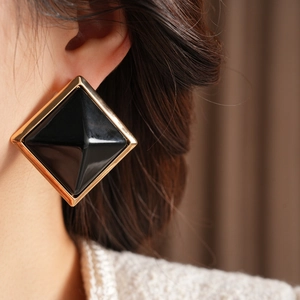 Close-up of geometric black resin square earrings with luxury polished gold metal frame
