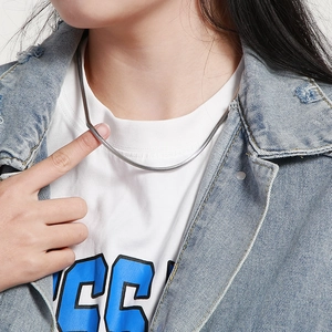 Close-up of a sleek silver snake bone chain necklace worn with a denim jacket