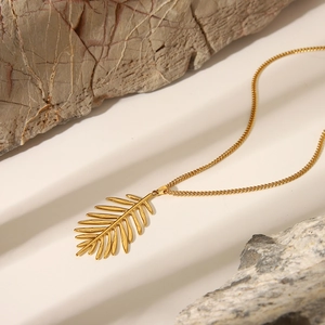 Detailed view of a gold leaf pendant necklace elegantly placed on natural grey stones
