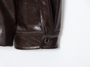 Detailed close-up of brown leather jacket cuffs featuring stitching and black metal snap buttons