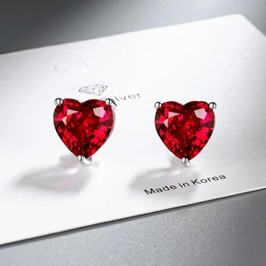 Macro shot of silver stud earrings with heart-shaped red zircon on white display card