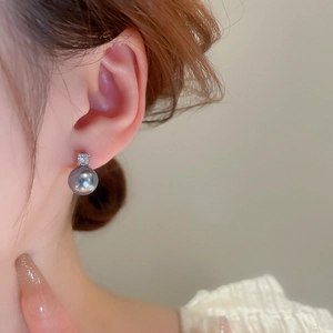 Detail view of a square crystal and grey pearl earring worn by a model