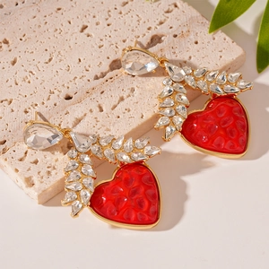Macro view of red resin heart earrings with gold trim and crystal leaf detailing