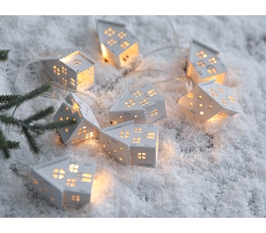 Close-up of warm white LED lights inside wooden miniature houses on a snowy winter background