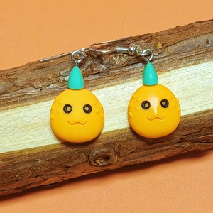 Close-up of handmade cartoon pumpkin earrings hanging on a natural wood stand