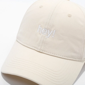 Detailed macro view of white hey embroidery on cream beige cotton baseball cap
