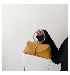 Detail of mustard yellow crossbody bag featuring a rhinestone ring handle and metal chain