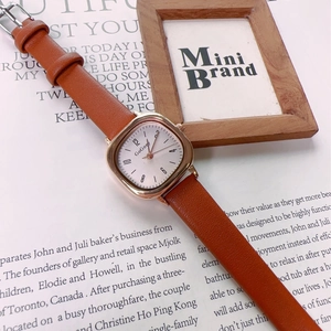 Detail of square gold-tone quartz watch with brown leather strap on vintage book pages