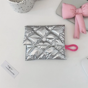 Close-up of a silver quilted makeup pouch with snap closure on a clean white desk