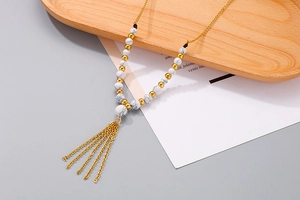 Dettaglio della collana con nappe dorate e perle di marmo su vassoio in legno