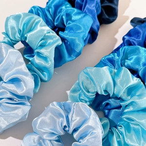 Detailed view of satin hair scrunchies showing glossy fabric texture in various blue tones