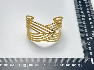 Dettaglio di un bracciale a fascia dorato con linee a V e trama perlata su una scala graduata