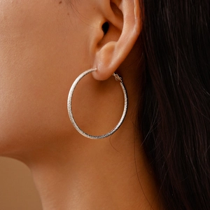 Close-up of matte silver hoop earring on model with textured finish and elegant design