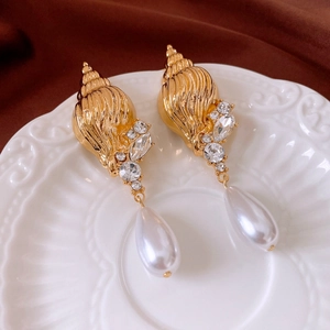 Detail of vintage golden conch earrings with white drop pearls and sparkling crystals