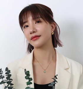 Close-up of a model wearing a gold necklace with an oval green cat-eye stone pendant