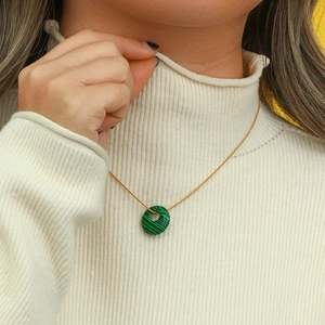 Close-up of green malachite round pendant necklace worn on a white turtleneck sweater