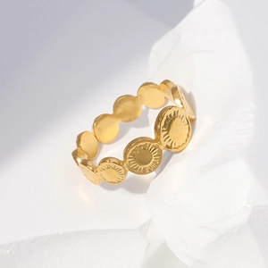 Detail of gold coin sun pattern link ring on a white textured stone surface
