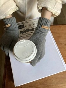 Close-up of grey knit cashmere gloves with brown leather label on a coffee cup