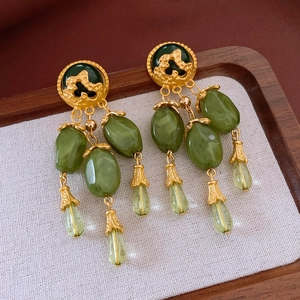 Detail view of vintage court-style tassel earrings with green gemstones on wooden tray