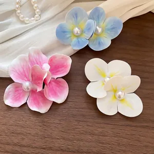 Elegant floral hair clips with pearls in pink, blue, and white on a dark wooden surface
