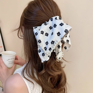 Detailed view of a floral bow hair clip with pearl trim on wavy hair, lifestyle setting