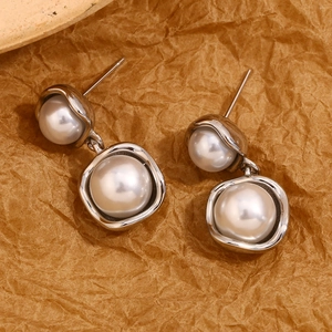 Macro detail of 316L stainless steel earrings featuring elegant white pearls on brown paper