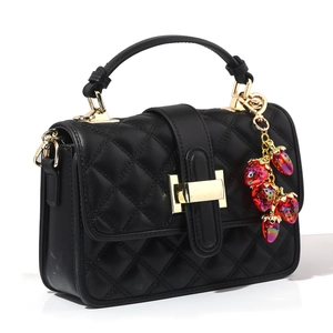 Detail of black quilted leather handbag featuring a red beaded strawberry charm and gold hardware