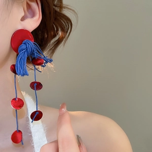 Macro view of long tassel drop earrings with red resin disks and blue woven rope texture